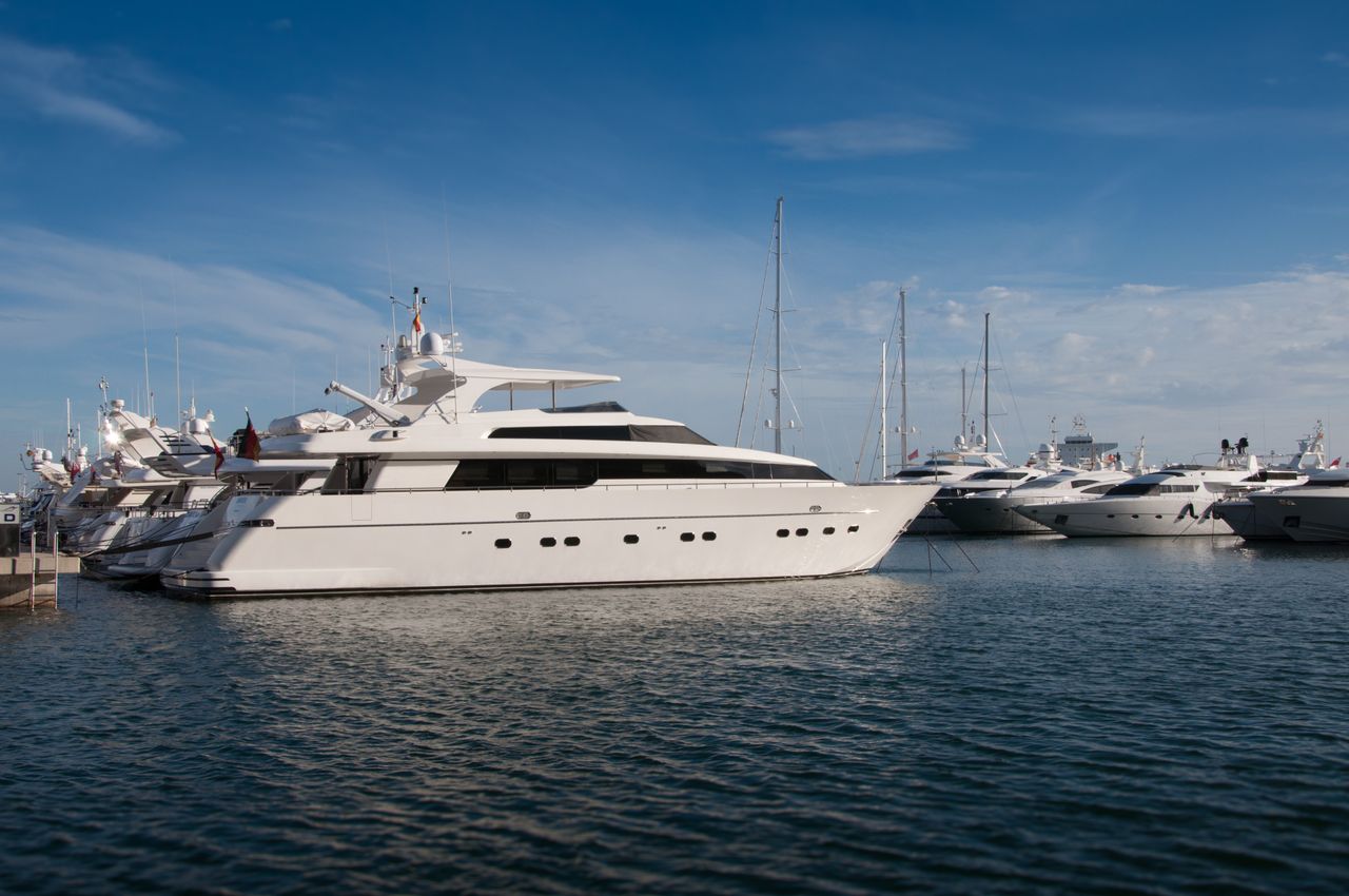 gallery-1 A serene marina scene featuring luxury yachts docked under a clear blue sky.